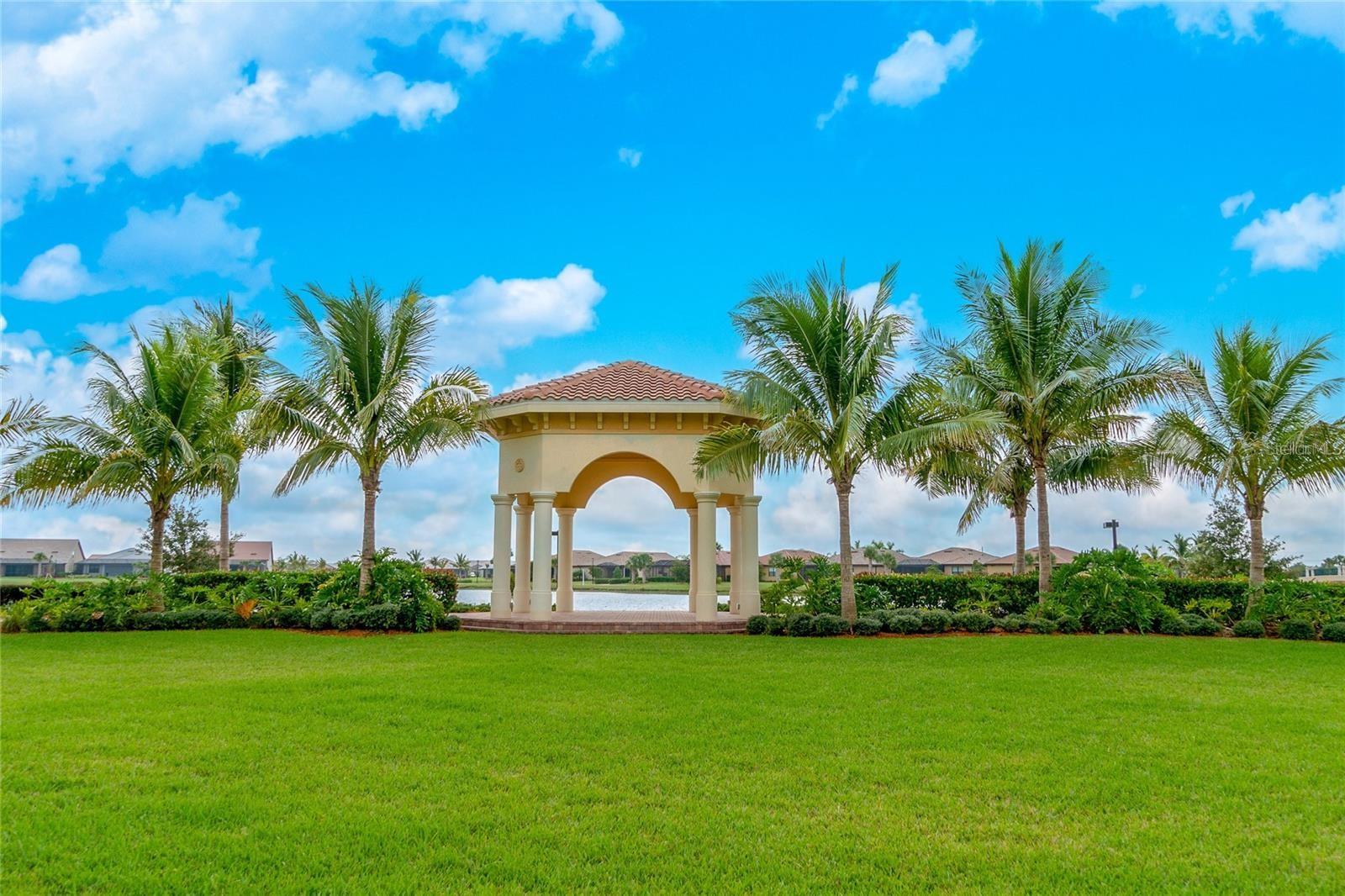 Community pavilion beside a pond, framed by palm trees and a broad green lawn.
