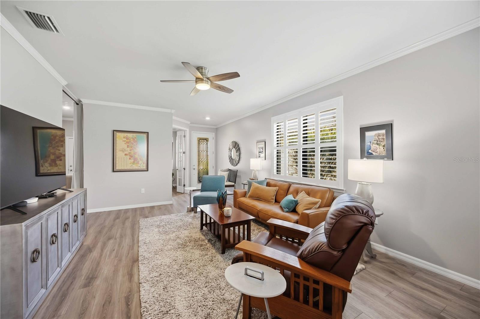 Furnished living room with leather sofa, plantation shutters, and ceiling fan.