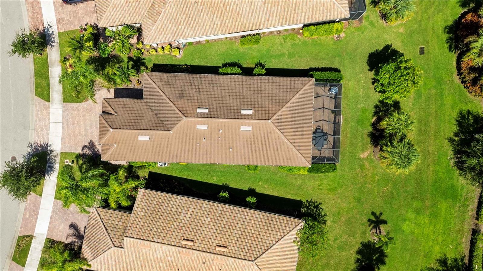 Aerial view of a tan-roofed home with a screened lanai and landscaped lawn.
