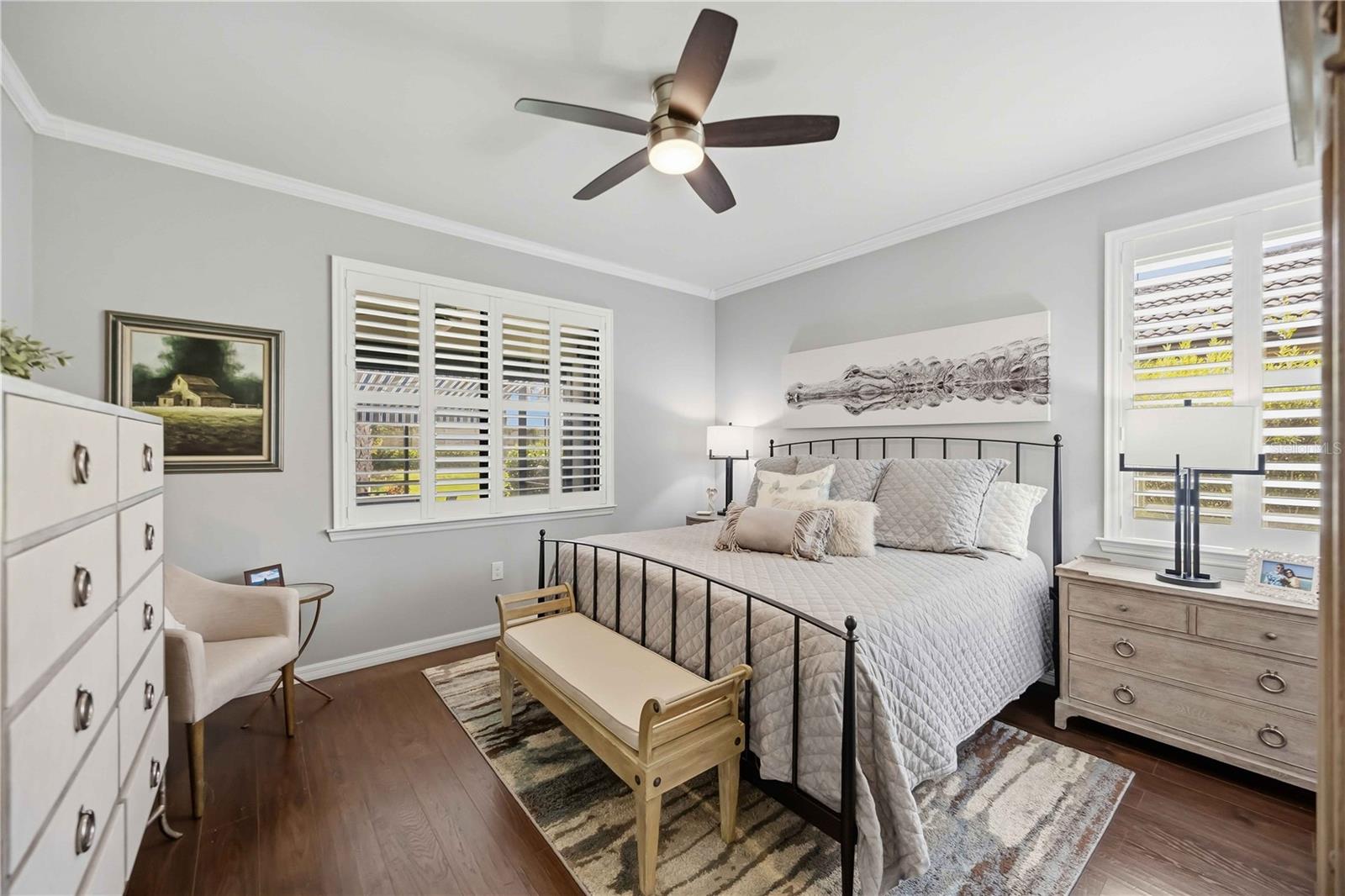 Bedroom with a black metal bed, plantation shutters, and a ceiling fan.