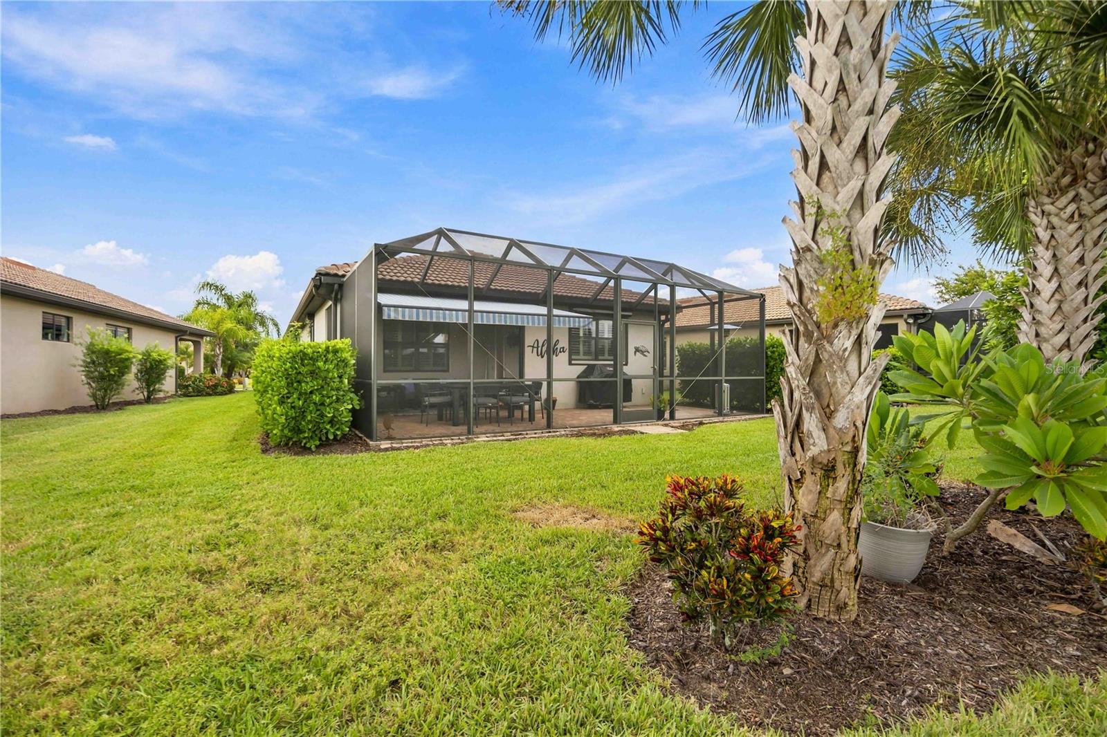 Rear of a single-story home with a screened lanai, patio furniture, and palm trees.