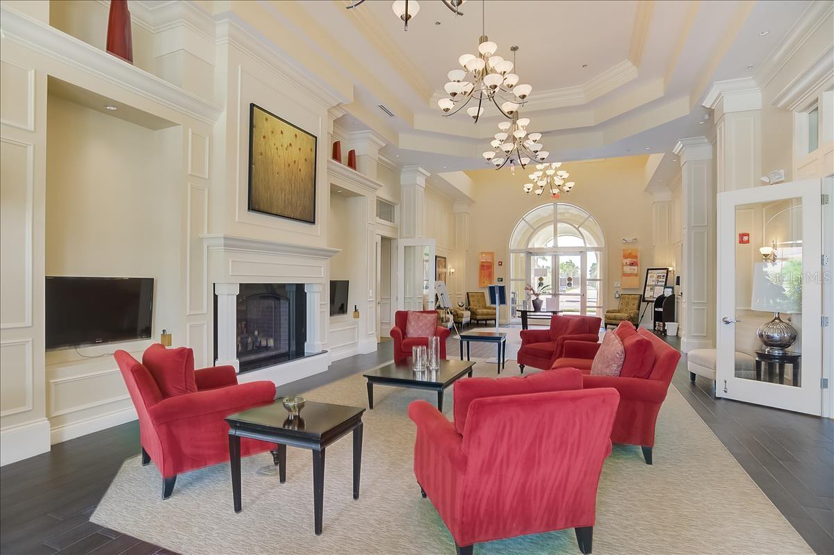 Community lounge with red seating, a white fireplace, chandeliers, and arched glass doors.