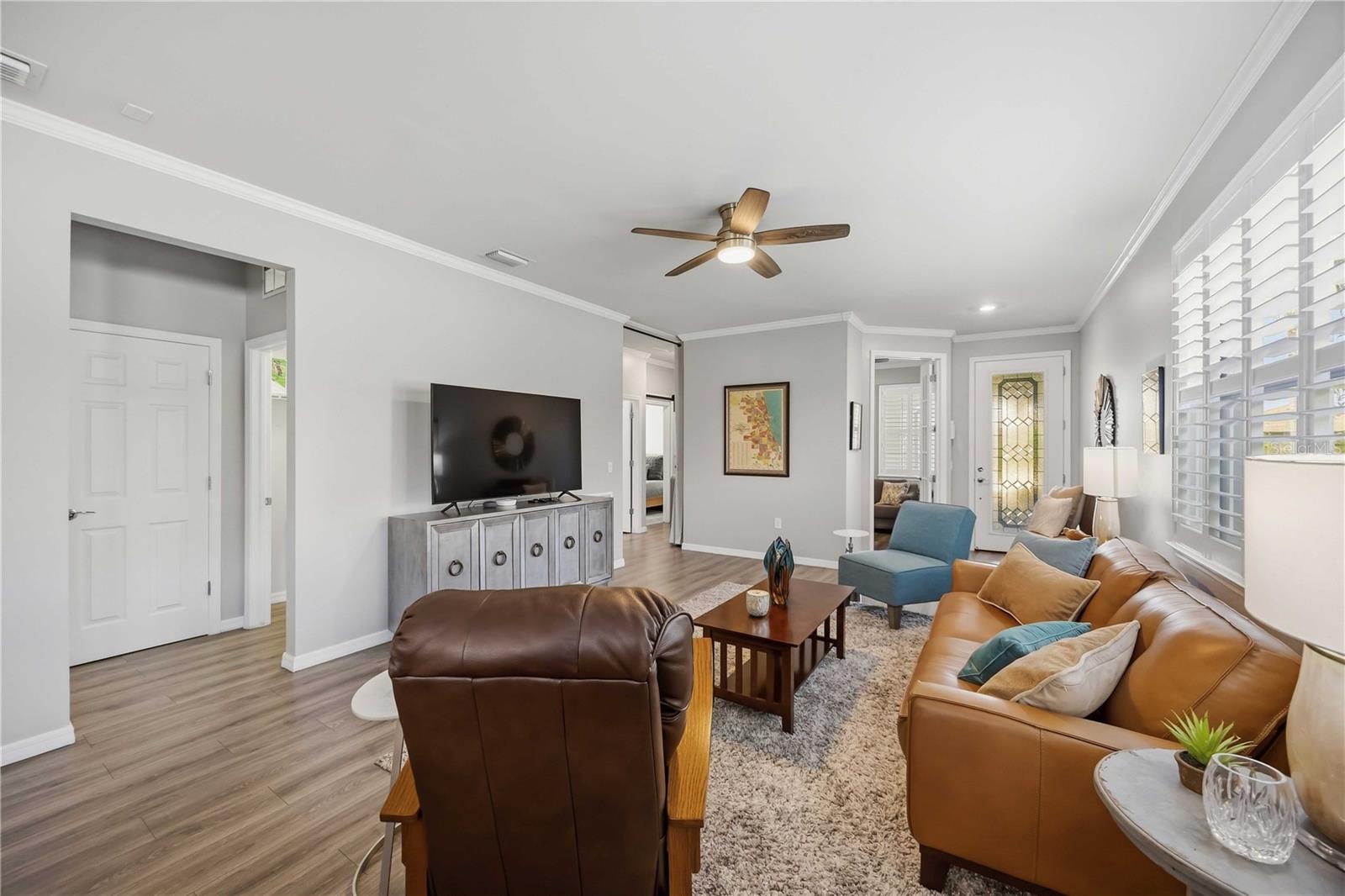 Furnished living room with leather sofas, a blue accent chair, and white-shuttered windows.