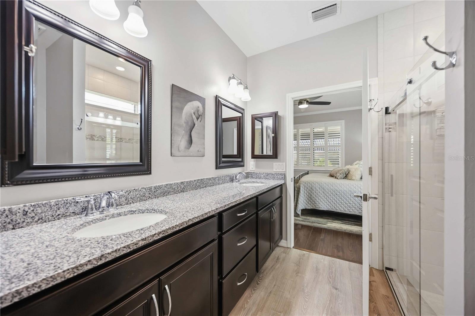 Primary bathroom with a granite double vanity, dark cabinetry, and a glass-enclosed shower.