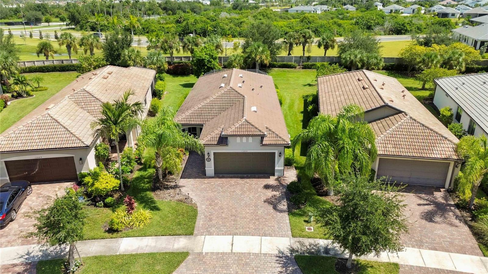 Aerial view of a tile-roofed home with palm landscaping and a brick-paver driveway.