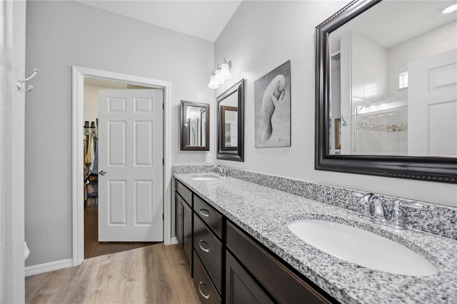 Bathroom with a long granite double vanity, dark cabinets, and framed mirrors.