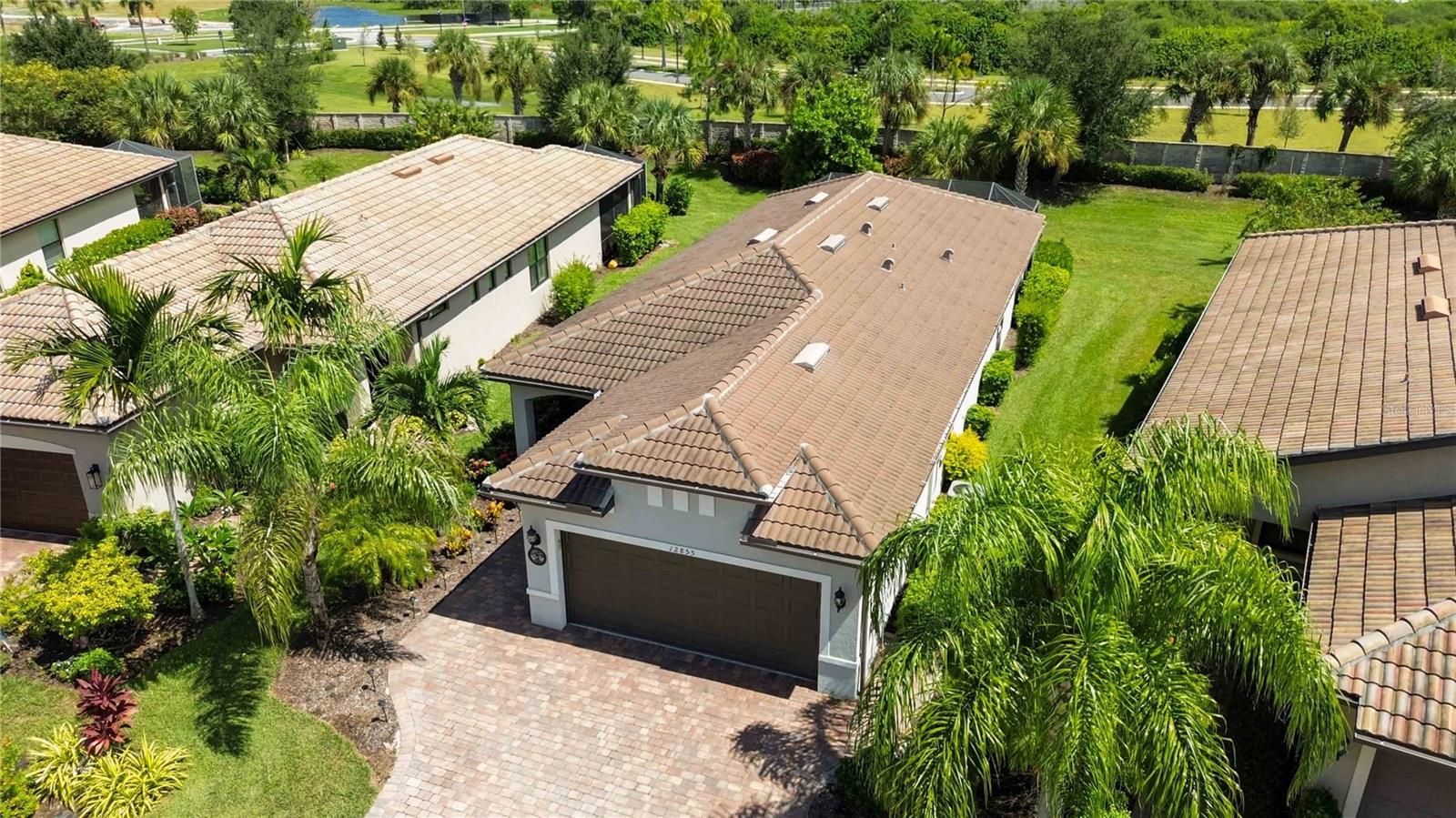 Aerial view of a tile-roof home with a paver driveway and tropical landscaping.