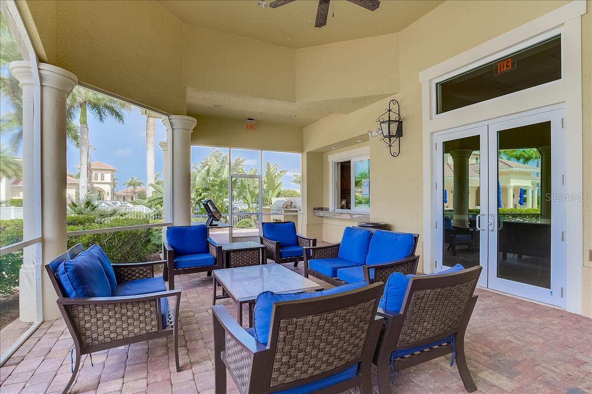 Covered patio with blue-cushioned wicker seating, paver flooring, and views of tropical landscaping.