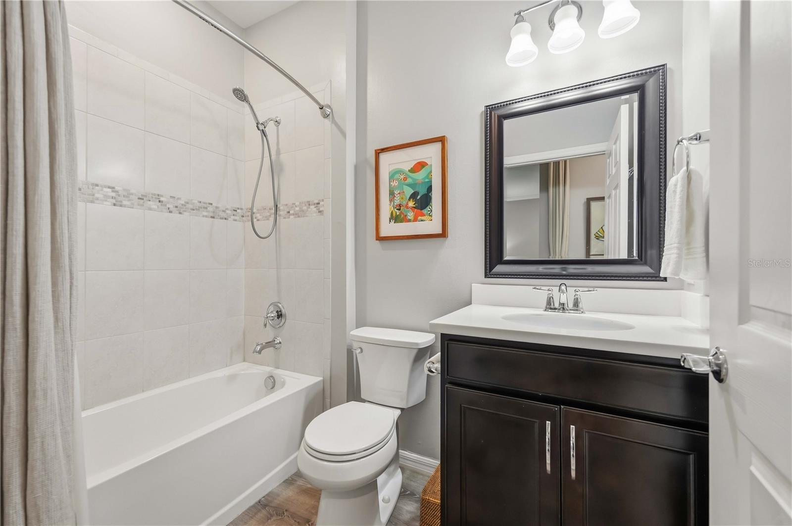 Bathroom with a tiled tub and shower, mosaic accent strip, and dark wood vanity.