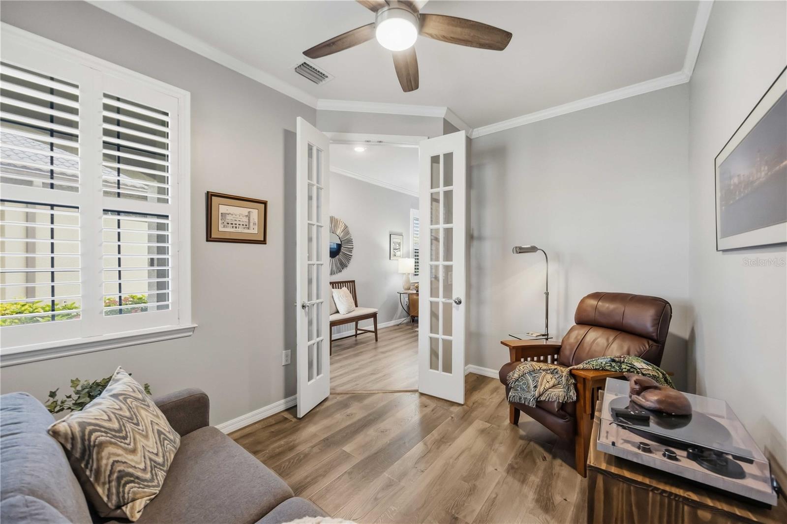 Living room with plantation shutters, a gray sofa, brown leather recliner, and open French doors.