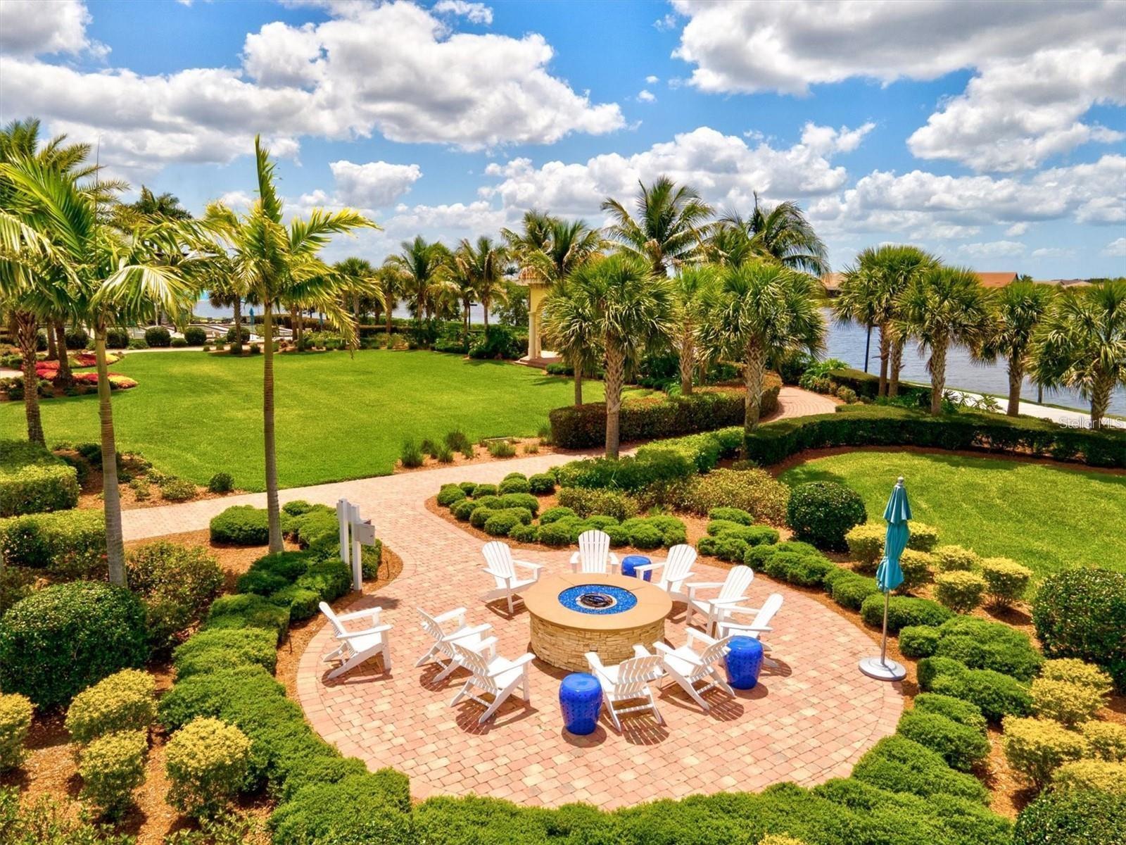 Waterfront courtyard with a brick fire pit patio, white chairs, palms, and landscaped lawn.