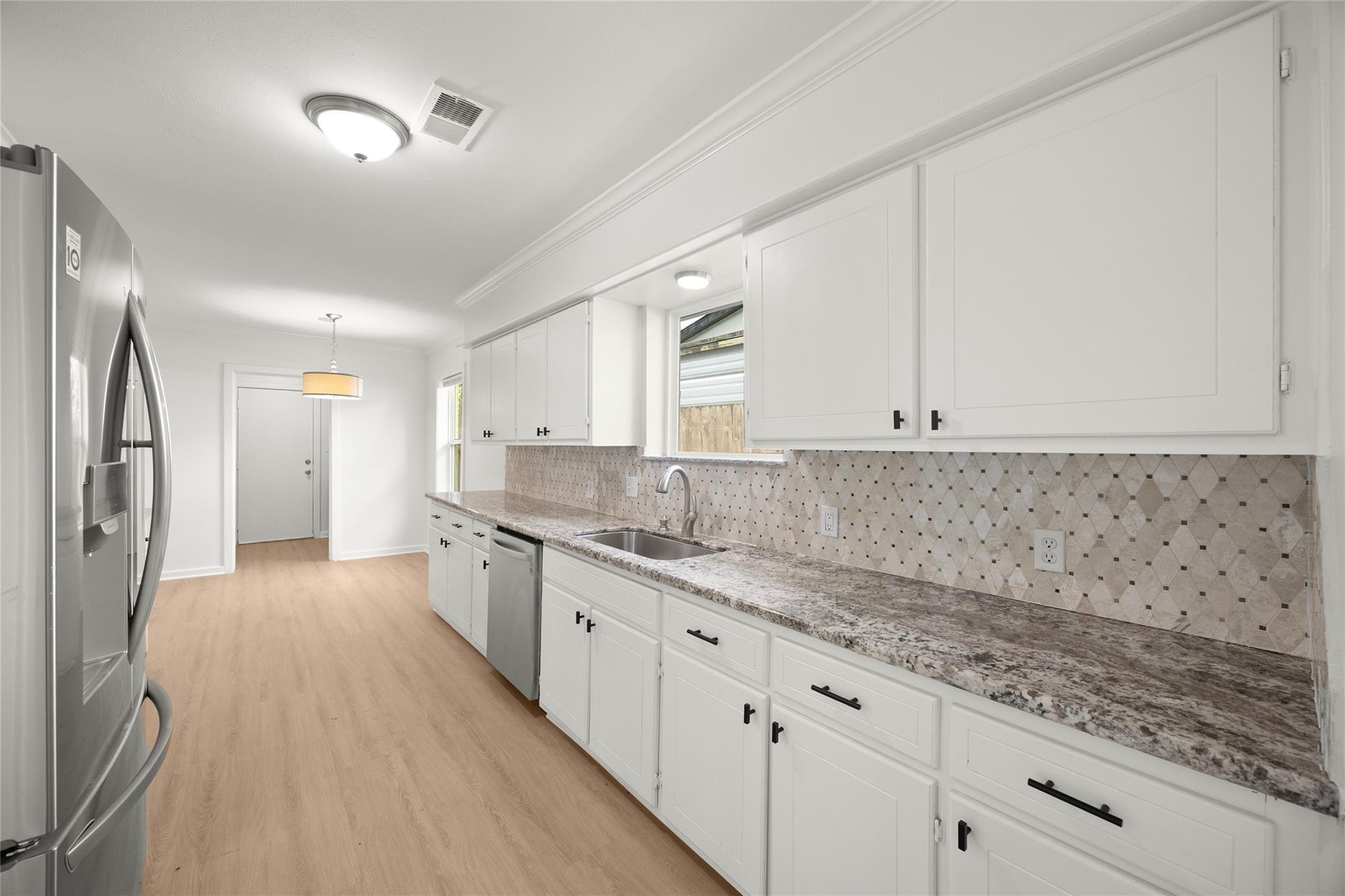 Kitchen with white cabinets, granite countertops, patterned tile backsplash, and stainless steel appliances.