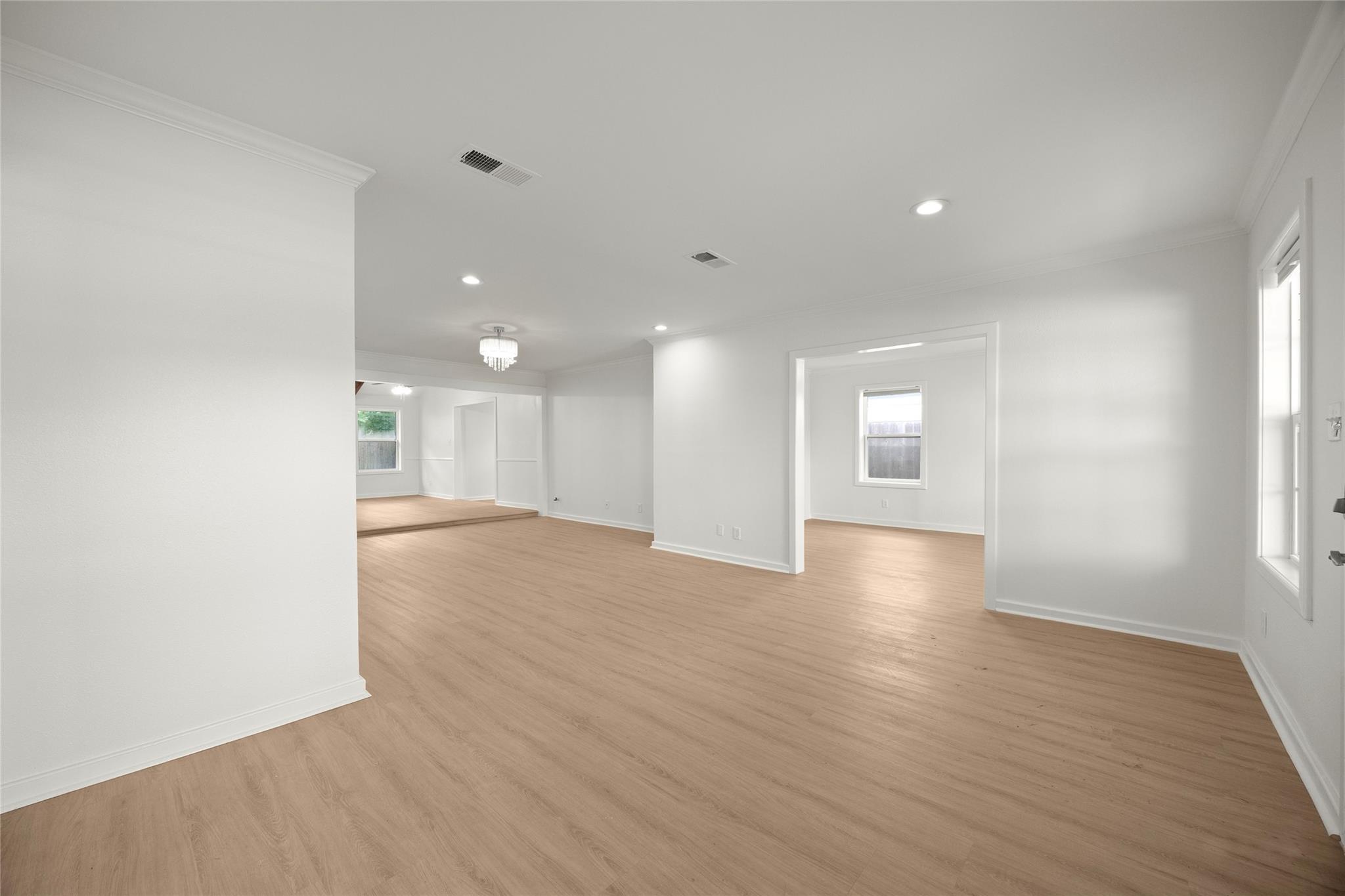 Empty living area with light wood floors, white walls, and wide openings to adjoining rooms.