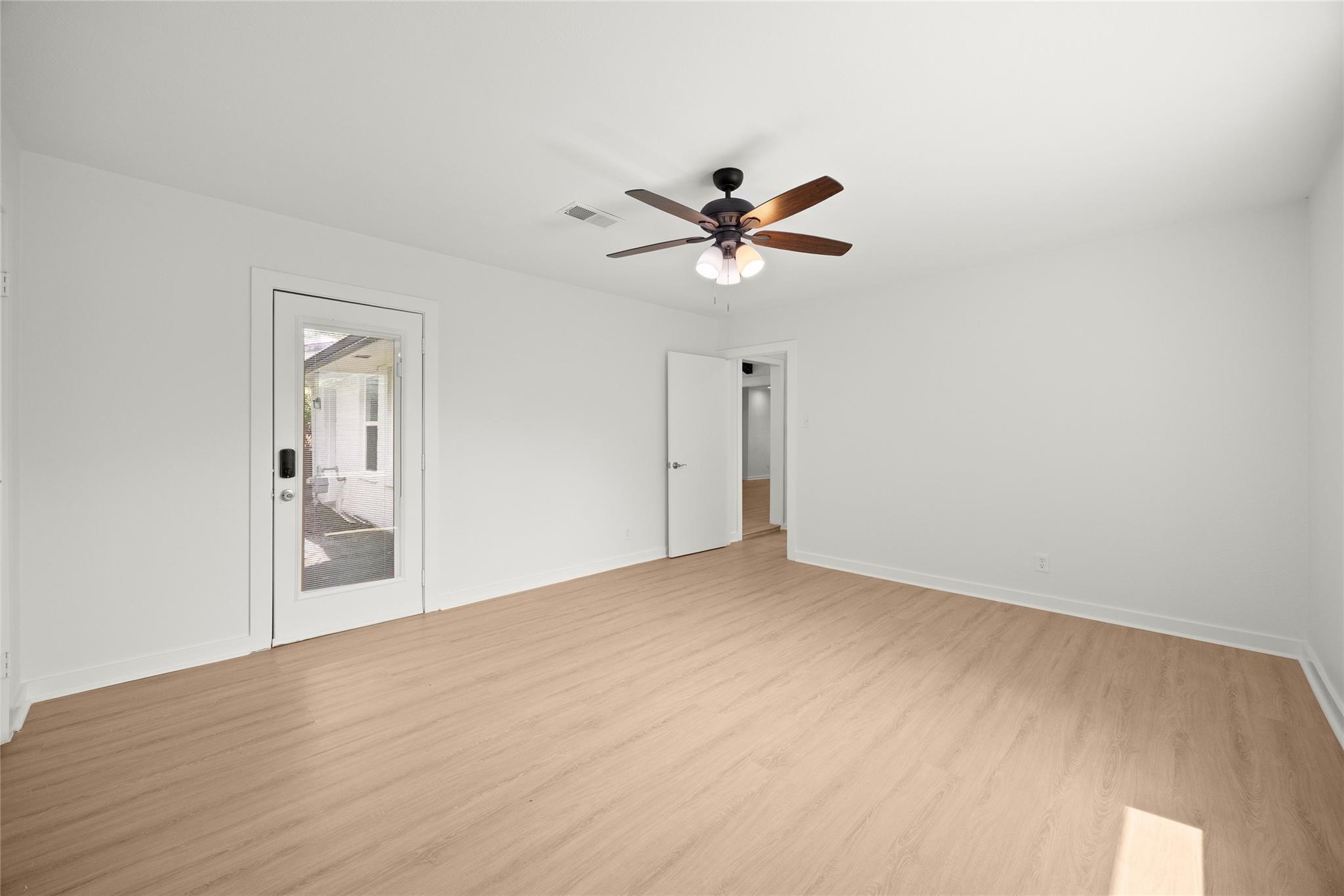 Empty room with light wood floors, a ceiling fan, and a glass door with blinds.