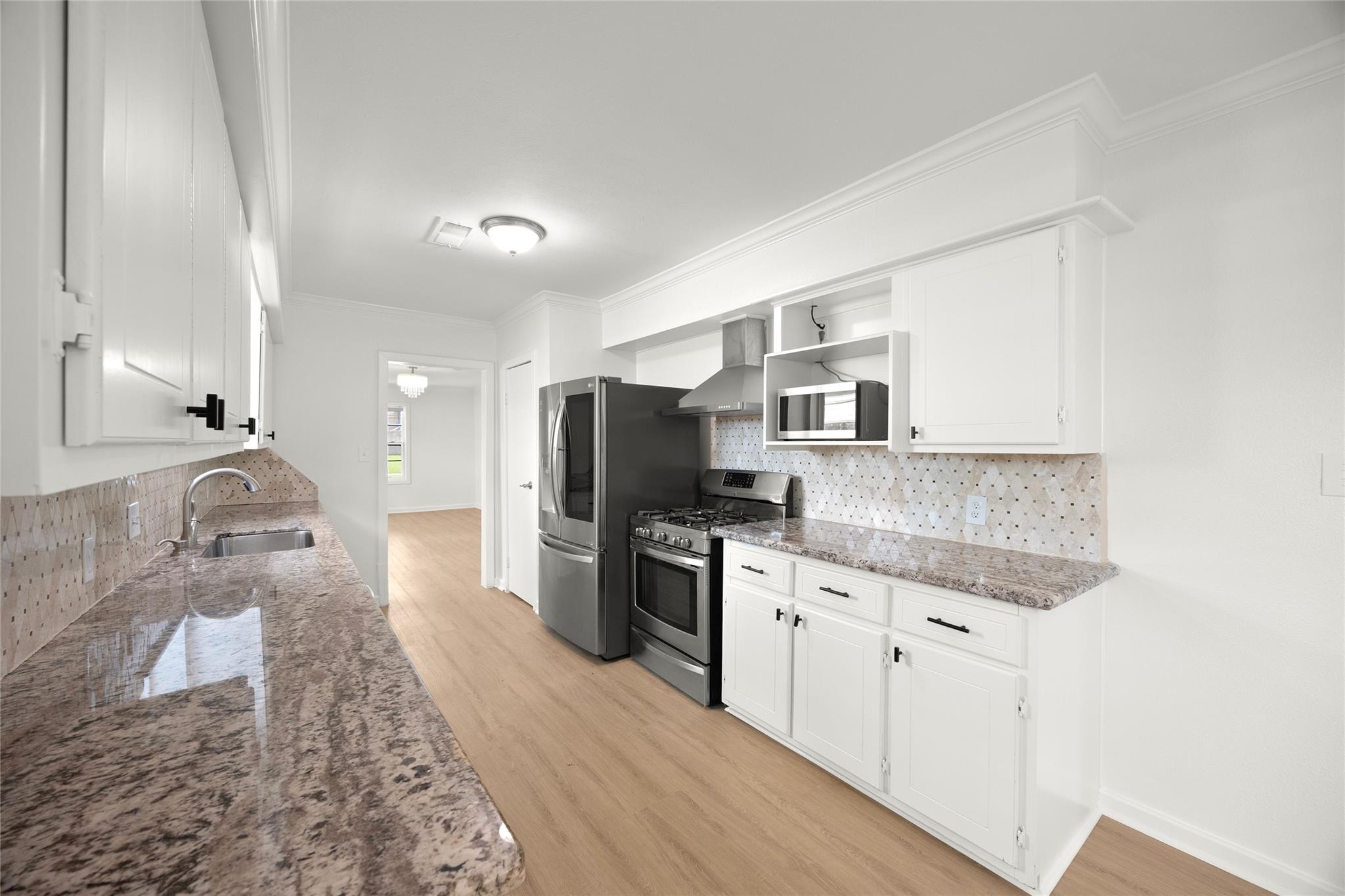 Kitchen with white cabinets, granite counters, patterned tile backsplash, and stainless steel appliances.