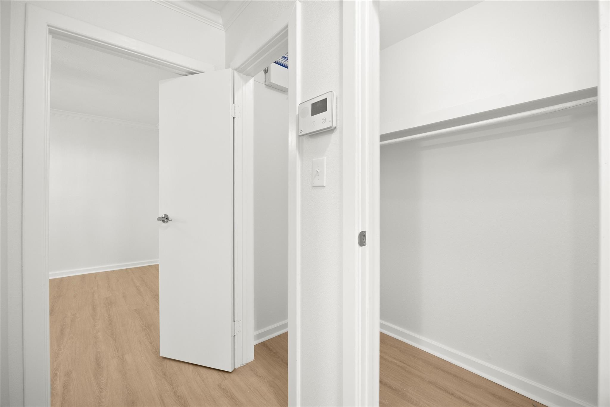 Empty closet with a single shelf and hanging rod beside an open doorway.
