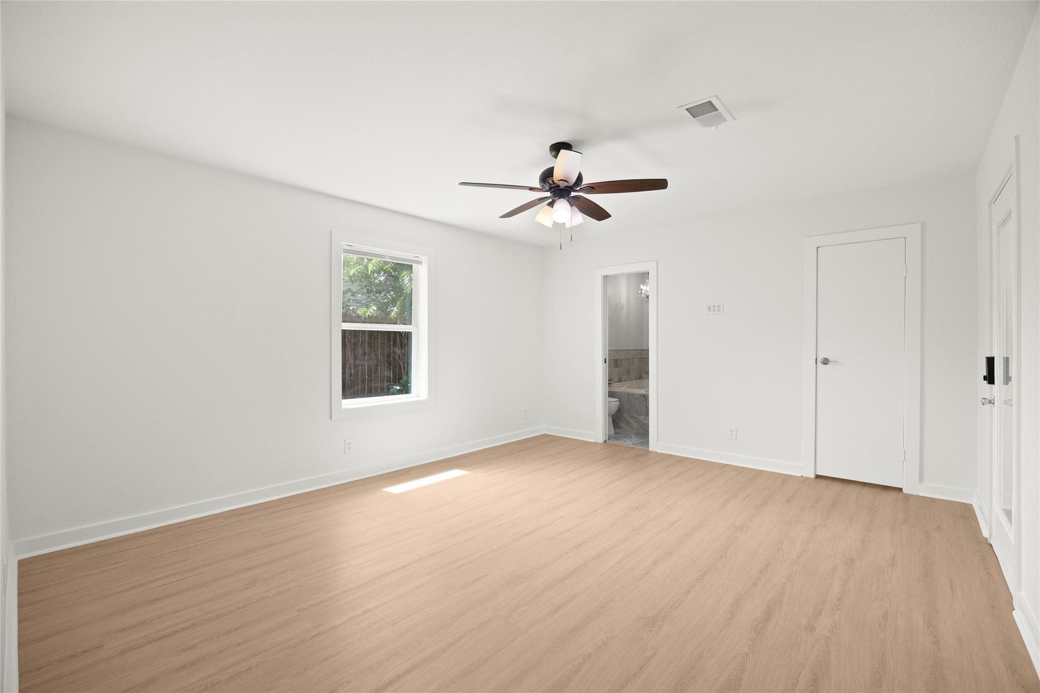 Empty bedroom with light wood floors, a ceiling fan, and an open doorway to the bathroom.