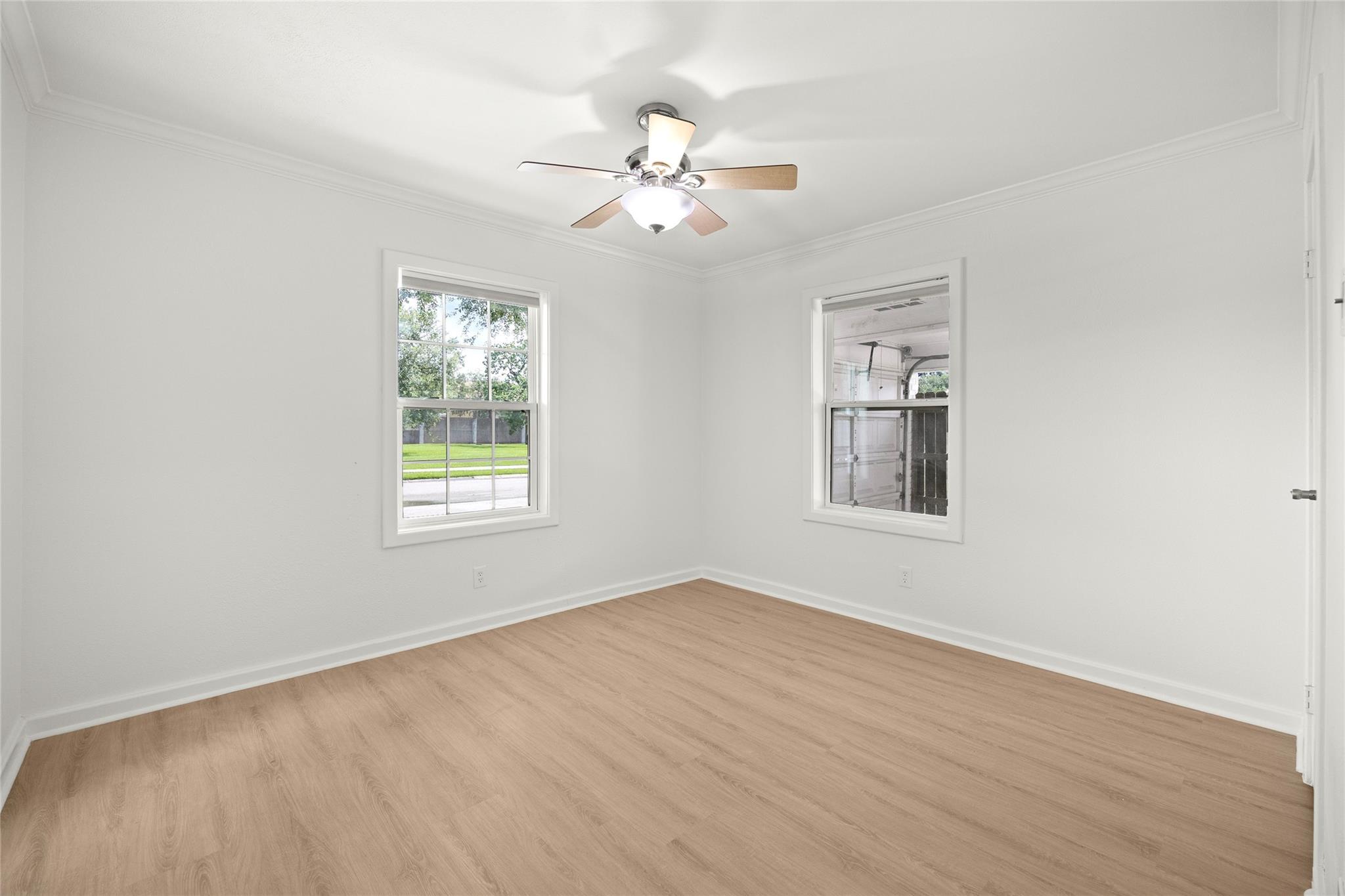 Empty room with light wood-look floors, two windows, and a ceiling fan with light.