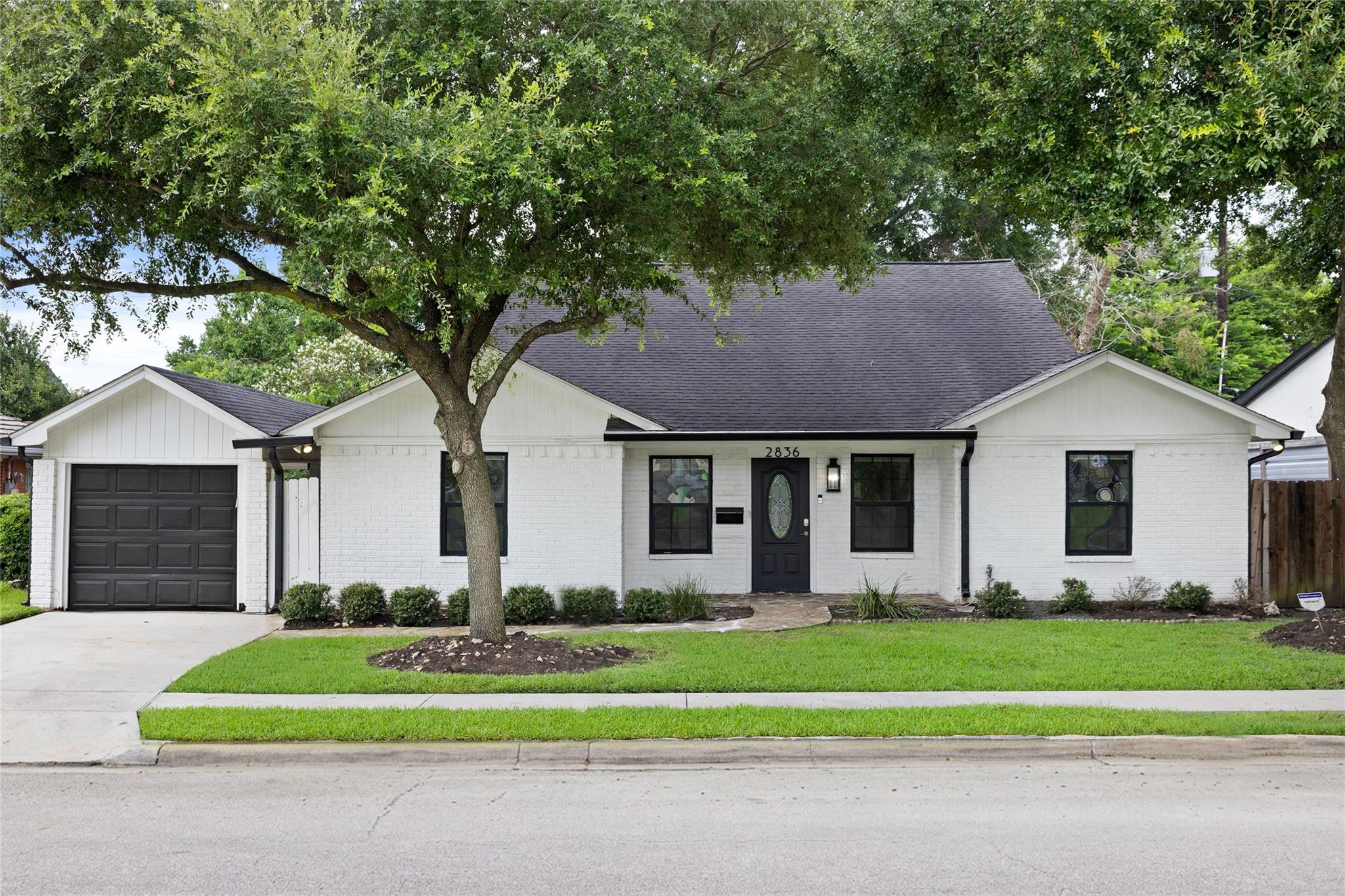 White brick home with a black garage door and large shade tree; house number 2836 above the entrance.