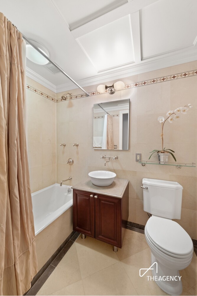 Bathroom with beige tile, a white tub, dark wood vanity, vessel sink, and orchid.
