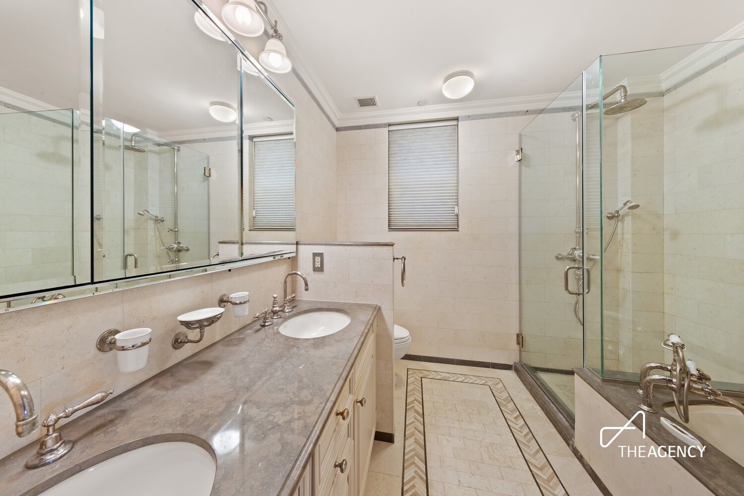 Marble bathroom with a double-sink vanity, mirrored wall, and glass-enclosed shower.