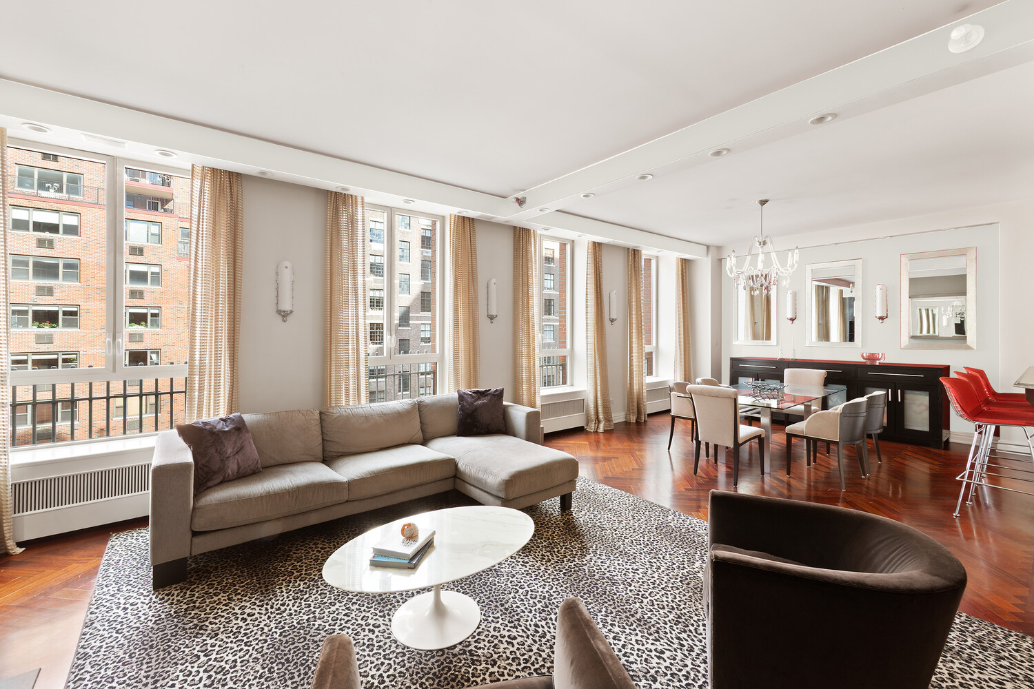 Furnished apartment living room with tall city-facing windows, gray sectional, and animal-print rug.