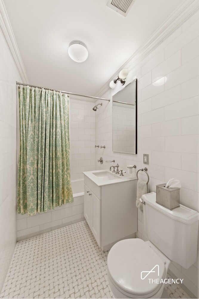 White-tiled bathroom with a green patterned shower curtain, vanity, and toilet.