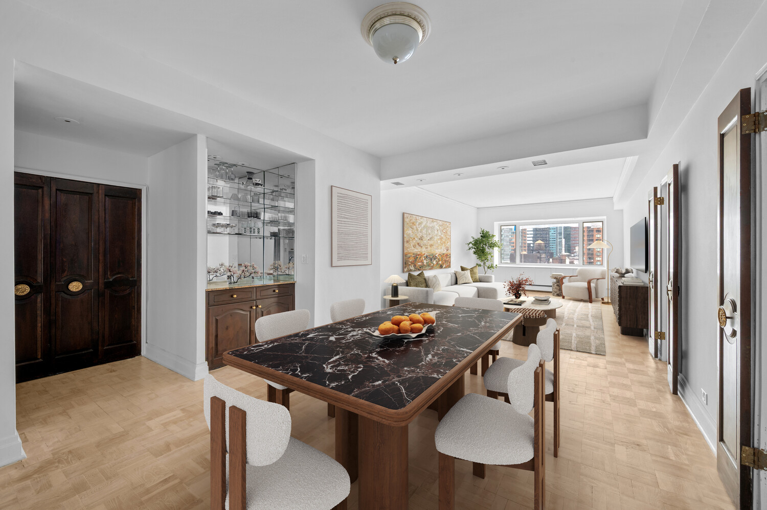 Open-plan apartment dining and living room with a dark marble table and city views through large windows.
