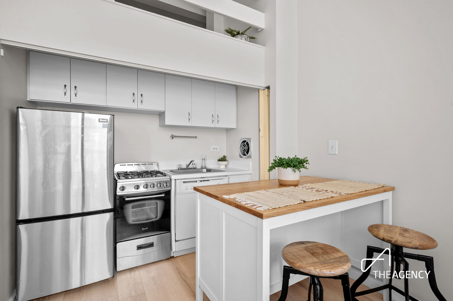 Compact kitchen with stainless steel appliances and a butcher-block island with two stools.