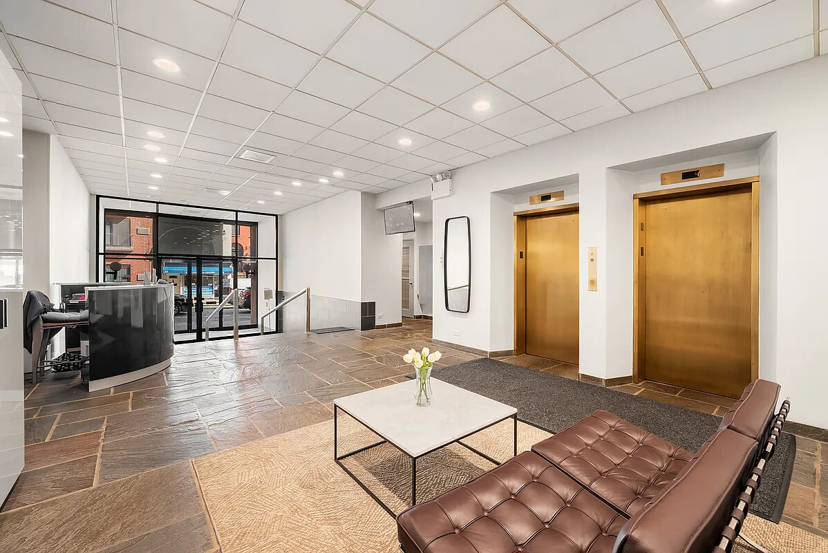 Building lobby with brass elevators, a curved reception desk, and brown leather seating.