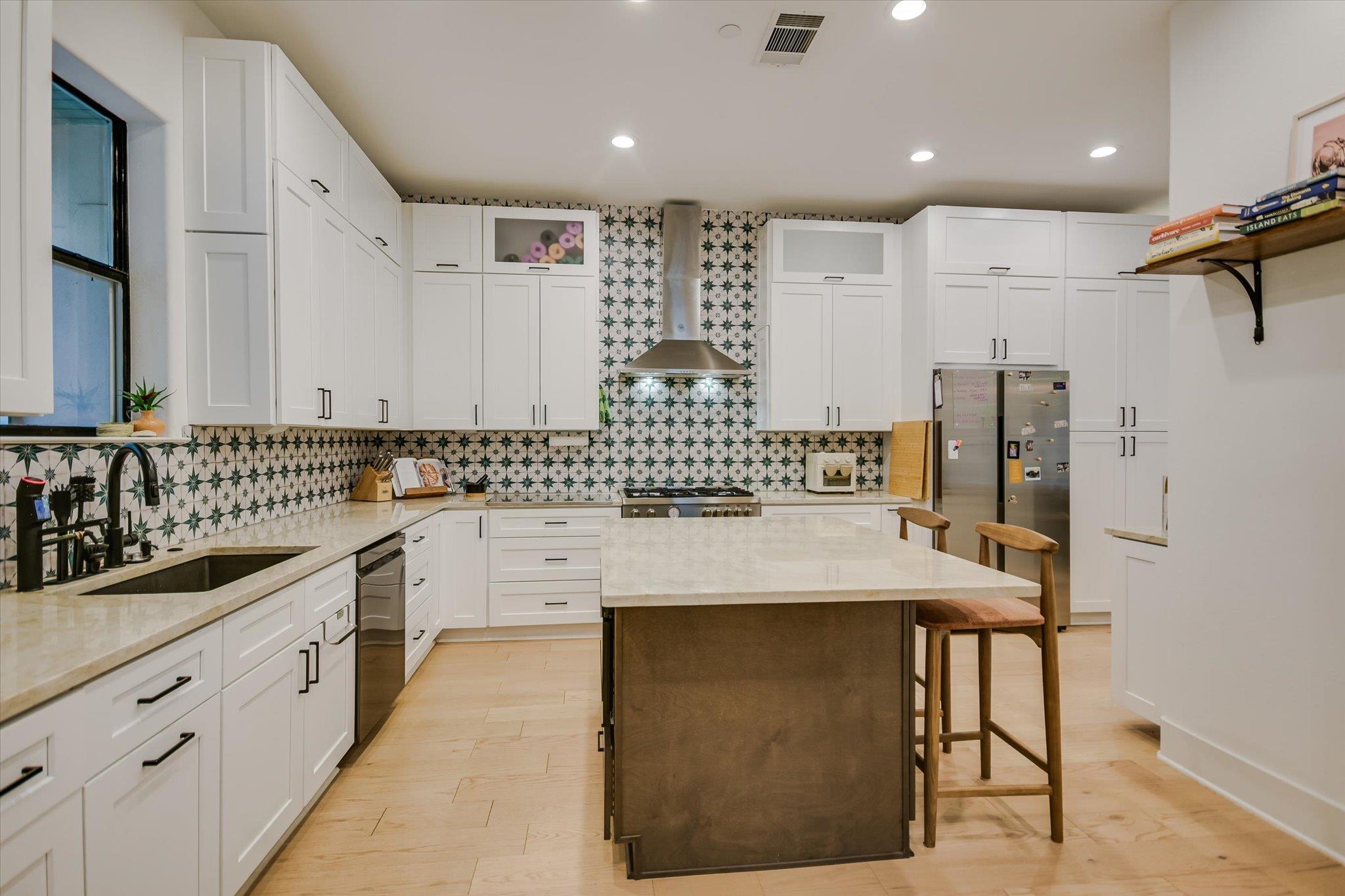 Kitchen with a large island, white cabinets, stainless appliances, and geometric tile backsplash.