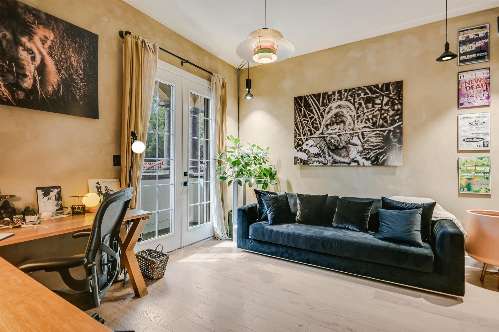 Living room and workspace with a blue sofa, wooden desk, French doors, and gorilla artwork.