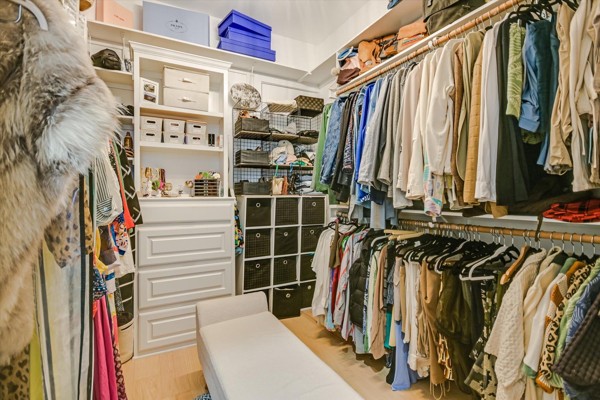 Walk-in closet with two tiers of clothing, built-in storage, and a padded bench.