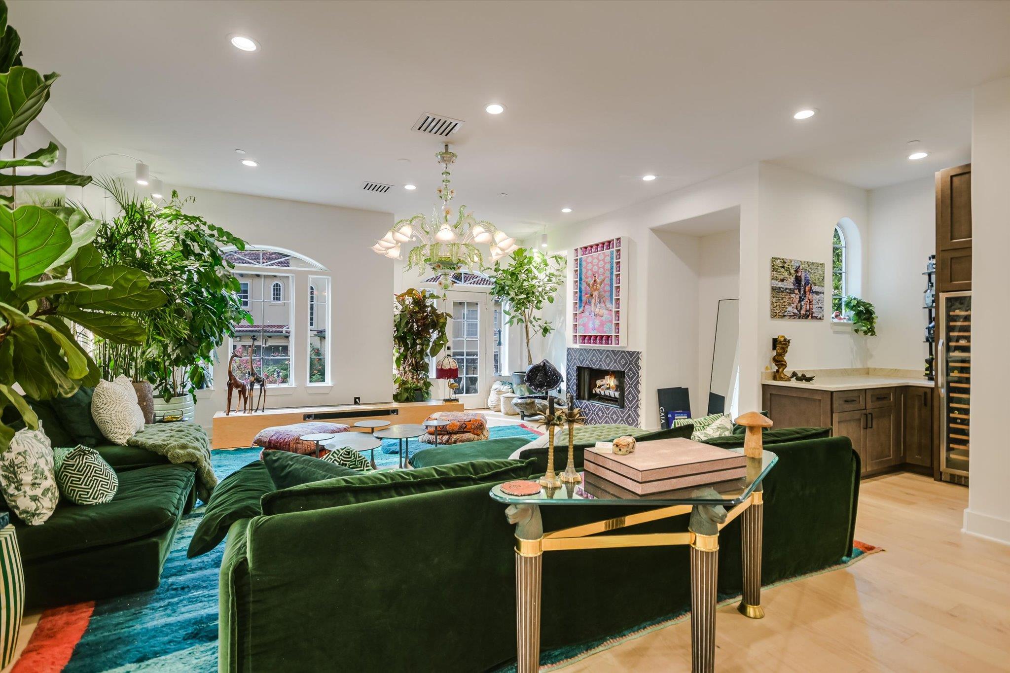 Living room with green velvet sofas, large windows, indoor plants, and a tiled fireplace.
