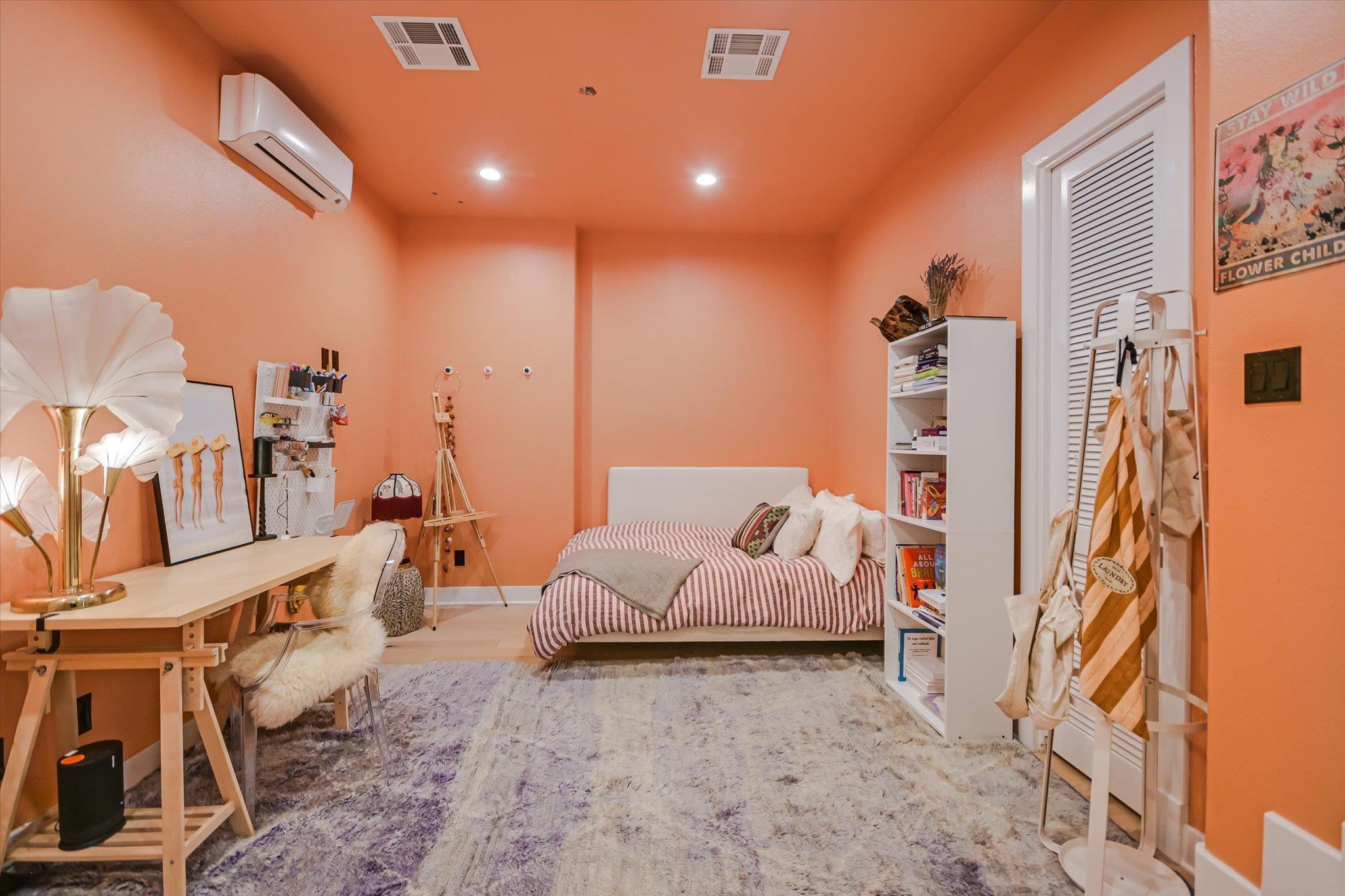 Bedroom with peach-orange walls, a striped bed, a desk, and a large shag rug.