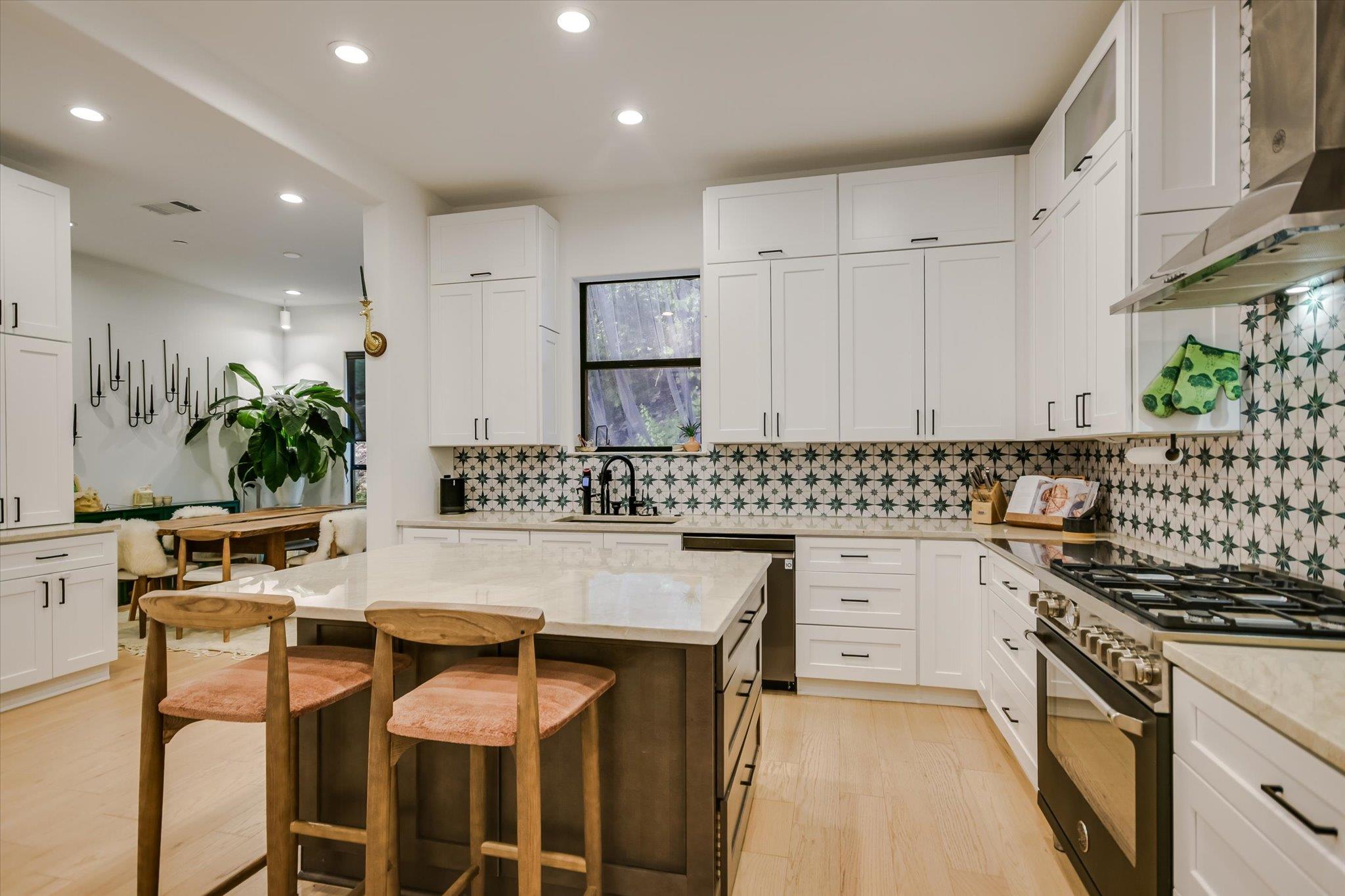 Kitchen with geometric tile backsplash, white cabinets, large island, and wooden stools.