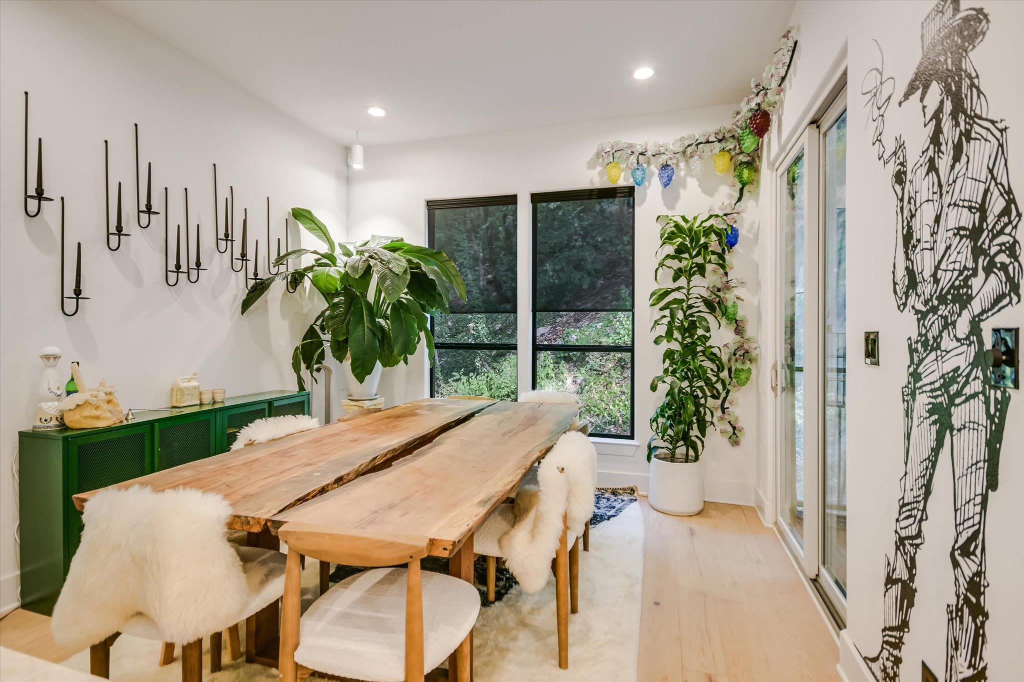 Dining room with a live-edge wood table, white chairs, large windows, and leafy plants.