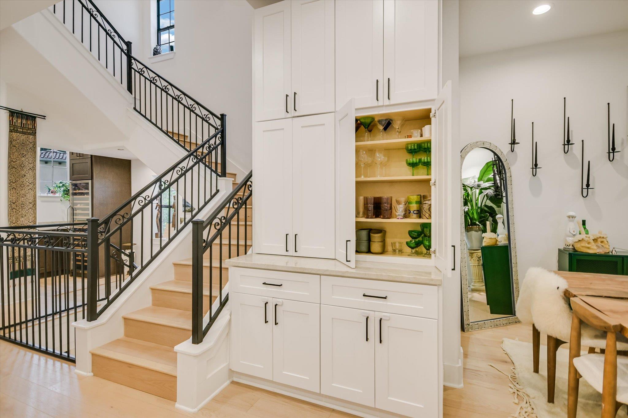 Light wood staircase with black railings beside white built-in cabinets displaying glassware.