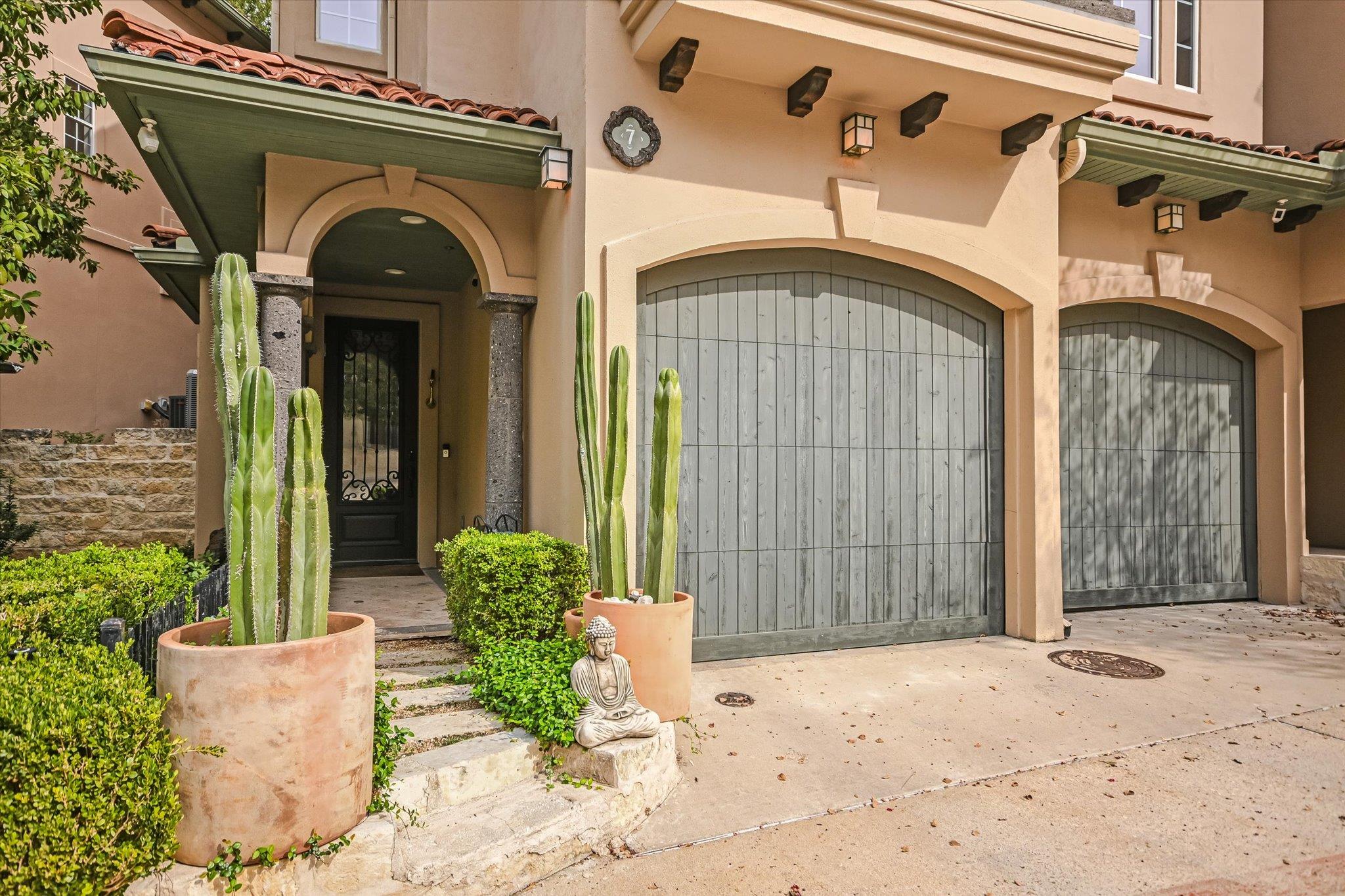 Tan stucco home with arched gray garage doors, a recessed entry, and potted cacti.