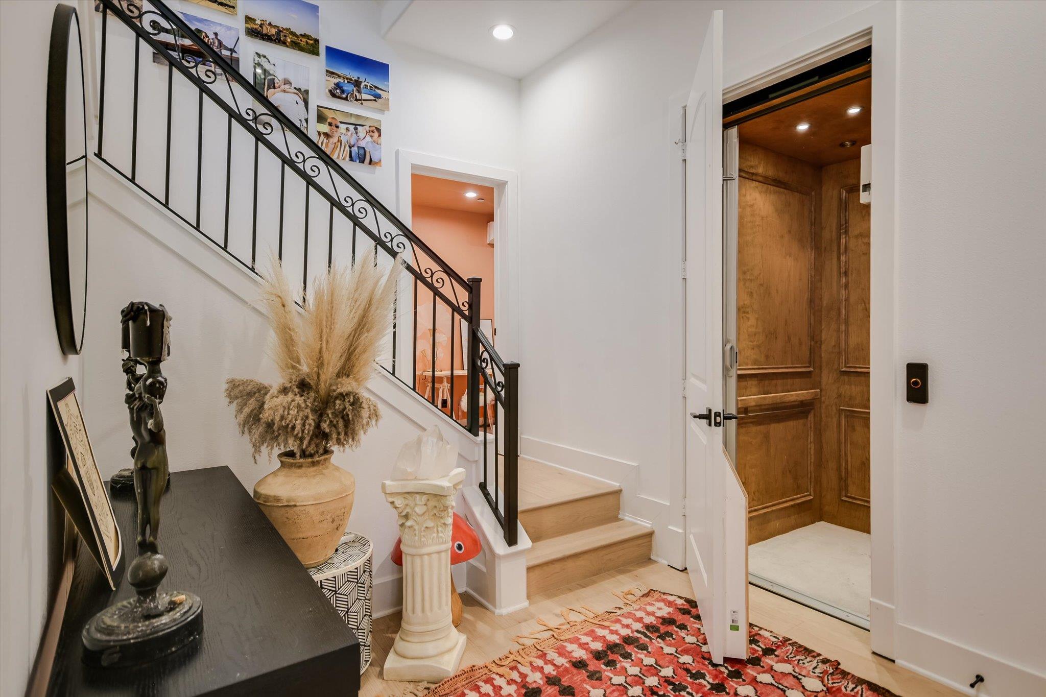 Entry foyer with an iron-railed staircase, patterned rug, and open wood-paneled elevator.