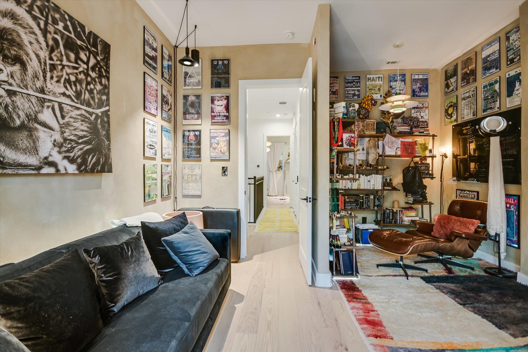 Living room with a dark sofa, poster-covered walls, bookshelves, and a brown leather lounge chair.