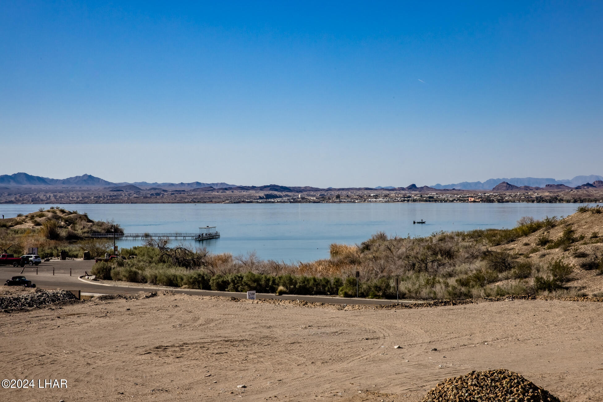 Vacant dirt lot overlooking a lake and distant mountain range.