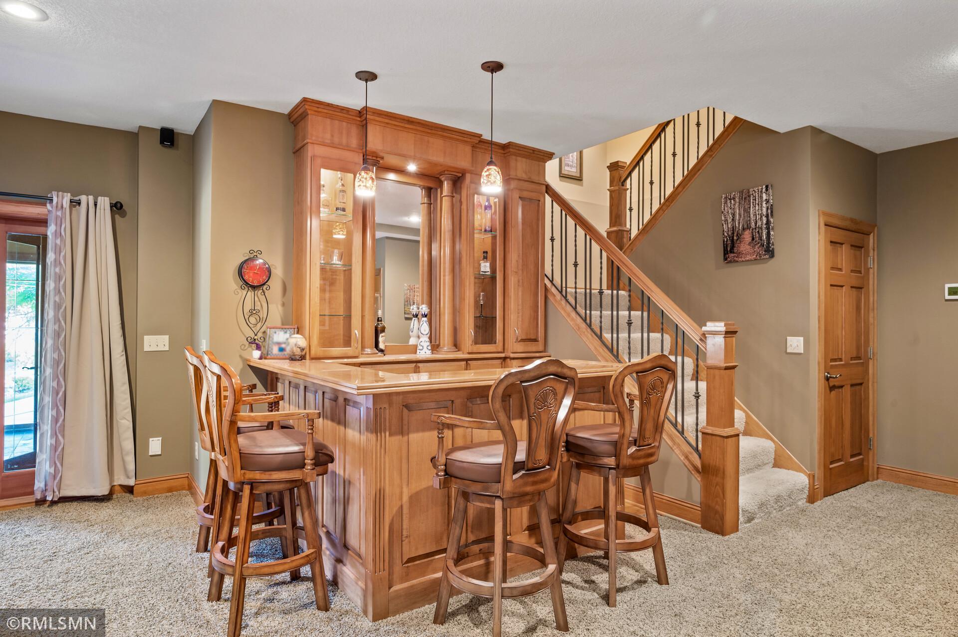 Built-in wood bar with glass-front cabinets and stools beside a carpeted staircase.