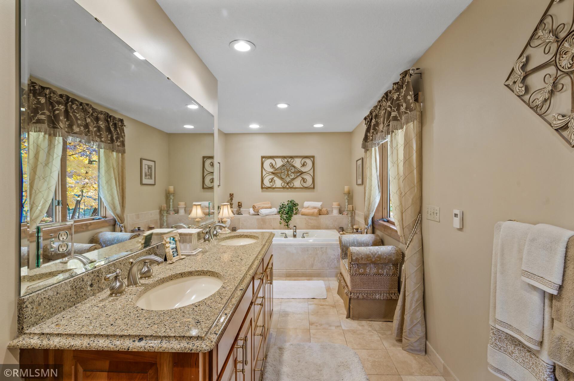 Primary bathroom with granite double vanity, large mirror, and soaking tub beneath decorative wall art.