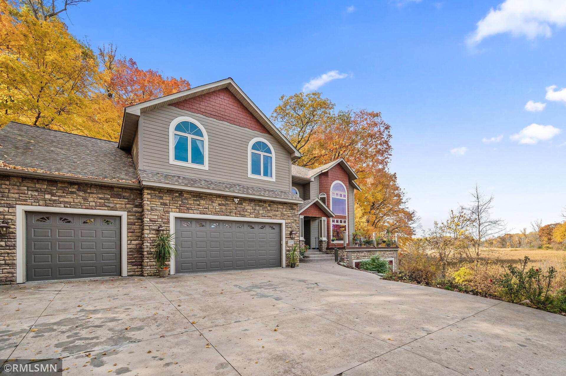 Two-story gray and stone home with red accents, two garage doors, and a broad driveway in autumn.