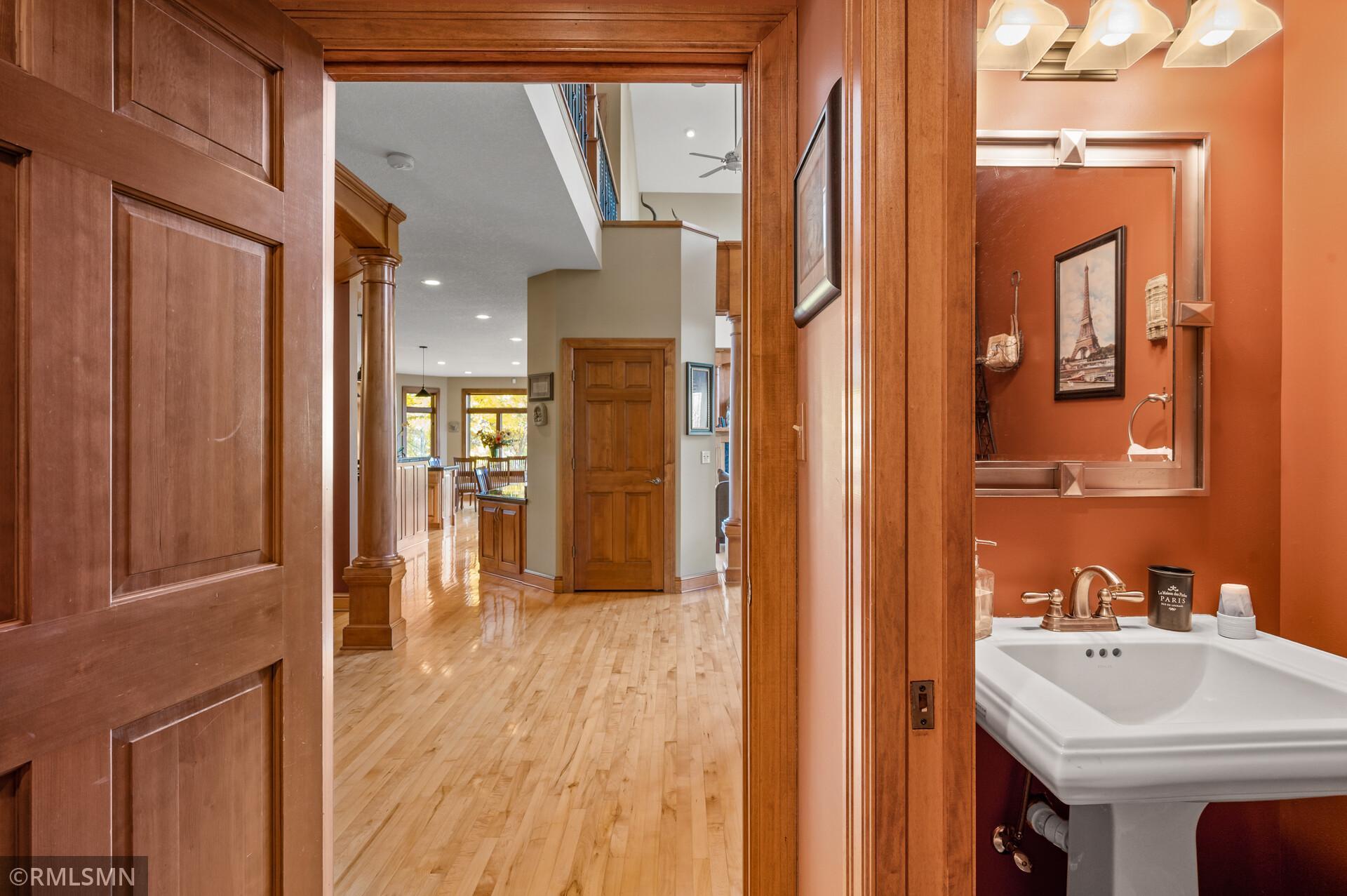 Wood-trimmed hallway with hardwood floors beside a terracotta powder room and white pedestal sink.