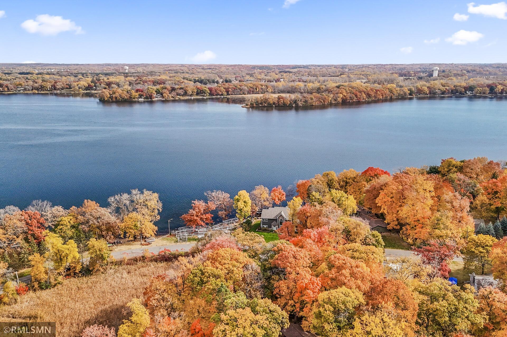 Aerial lake view with colorful autumn foliage, a wooded peninsula, and lakeside homes.