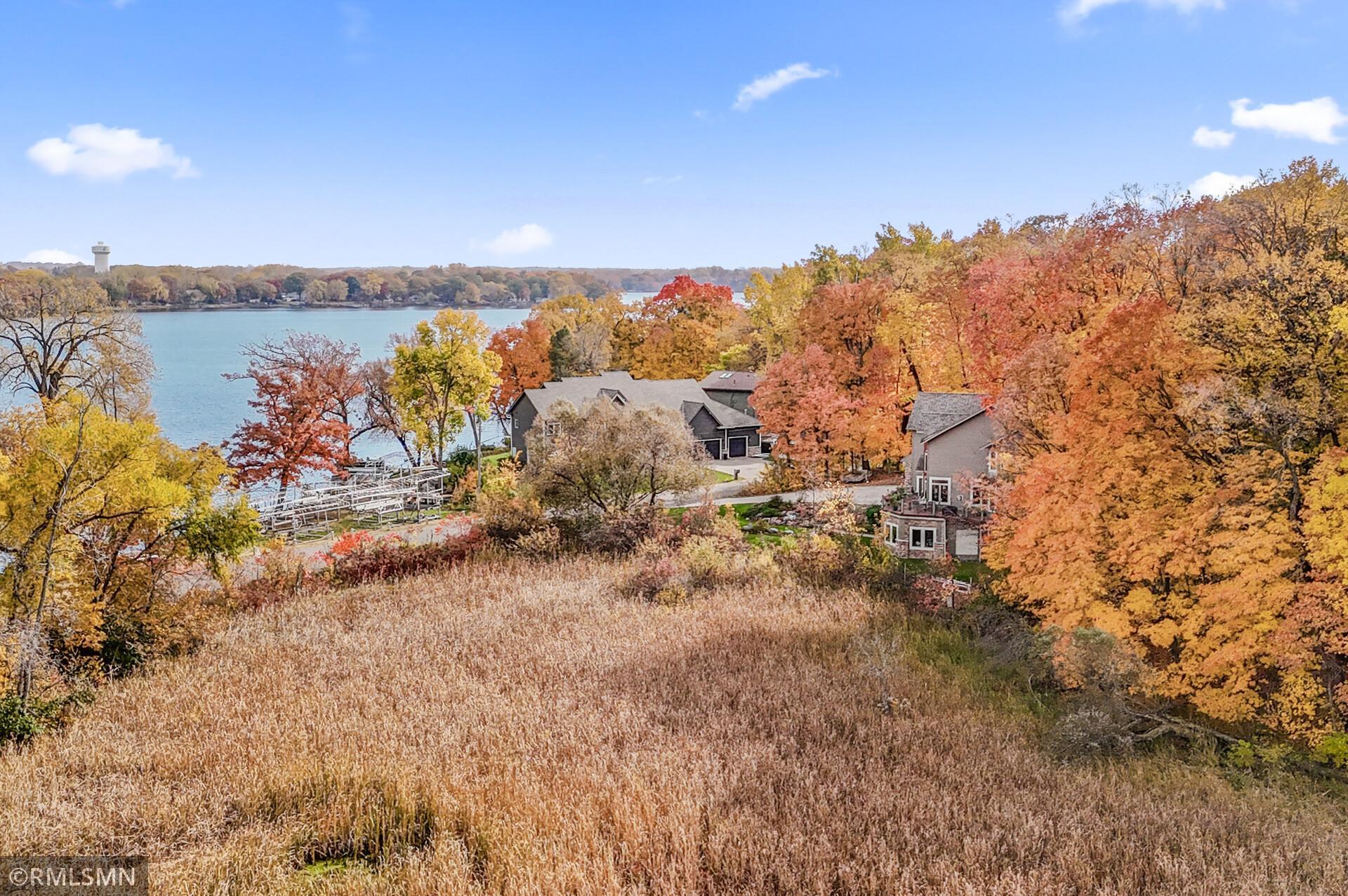 Aerial view of lakeside homes among autumn foliage, with a dock and broad lake view.