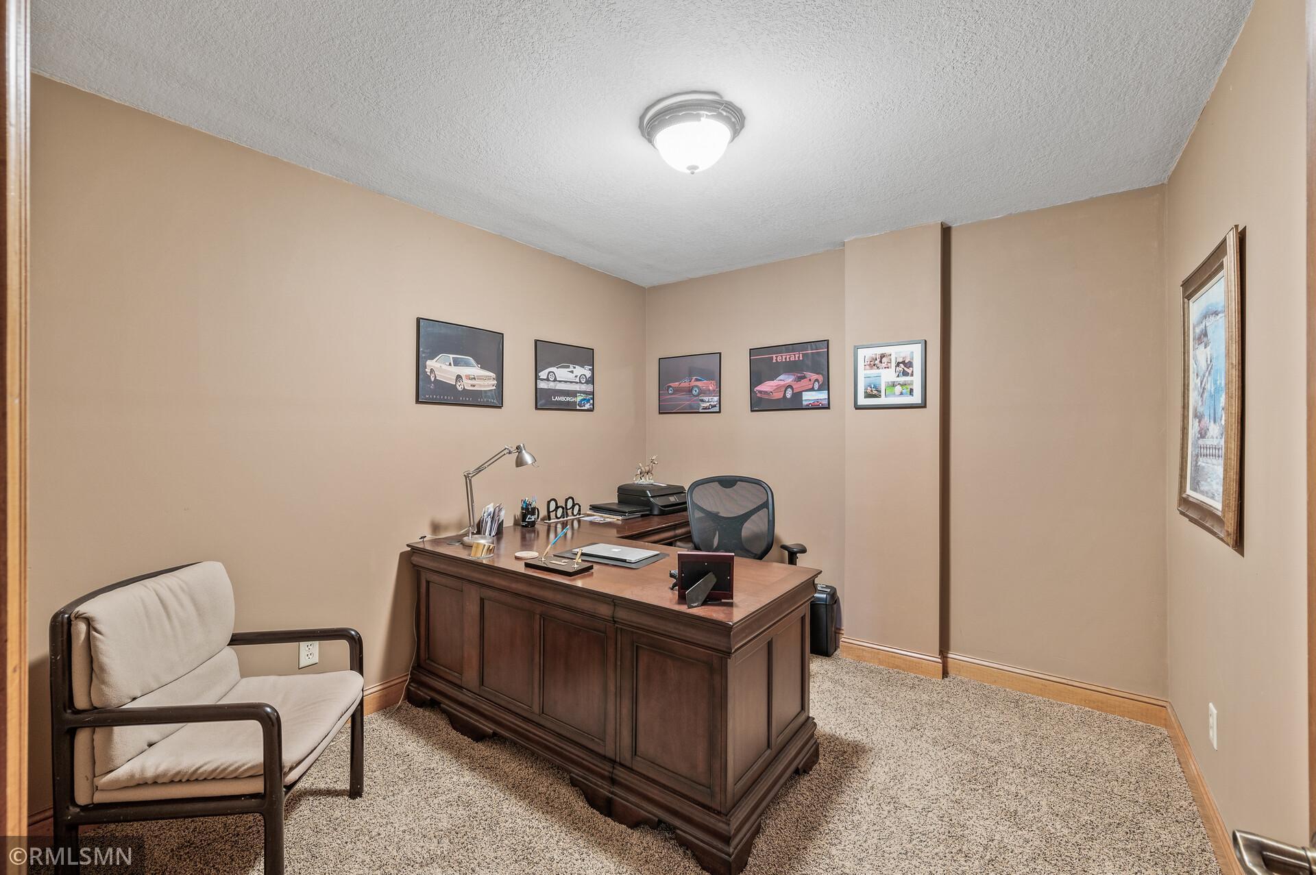 Furnished home office with a dark wood desk, guest chair, and framed car posters.