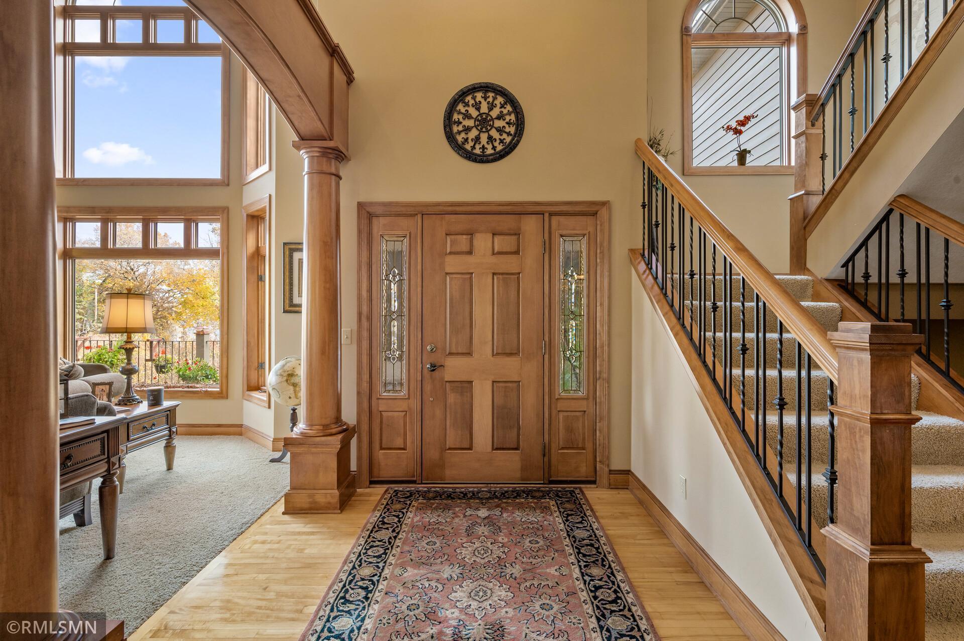 Foyer with a wood entry door, tall windows, and a carpeted staircase with wood railings.